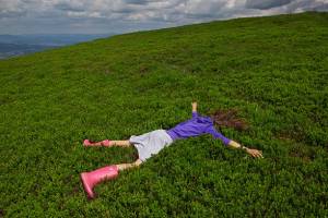 Girl lying facedown on the green bluberry field in the Carpatian mountain